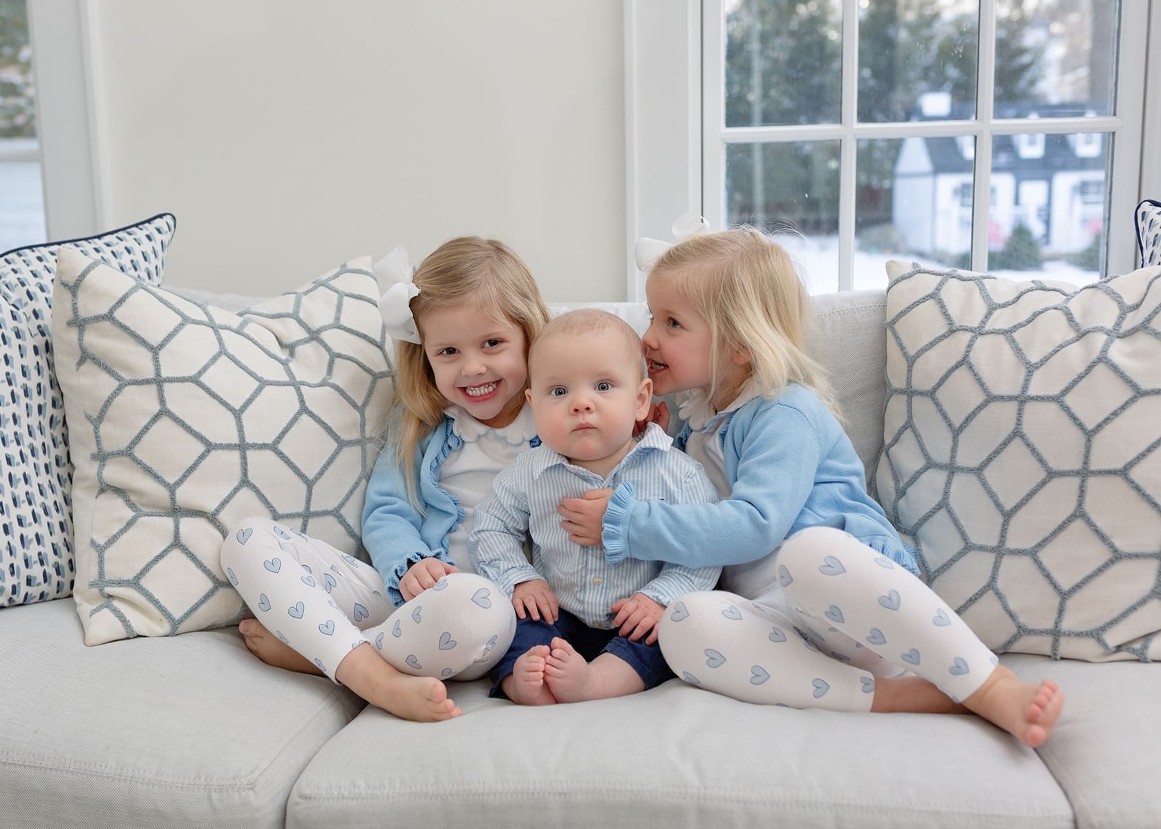 Two sisters on a couch with their baby brother sandwiched between them
